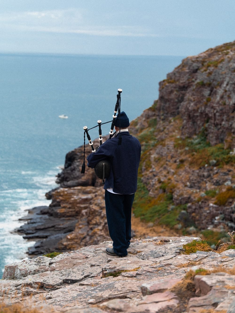 Le sonneur de dos, debout au bord de la falaise, la mer en contrebas.