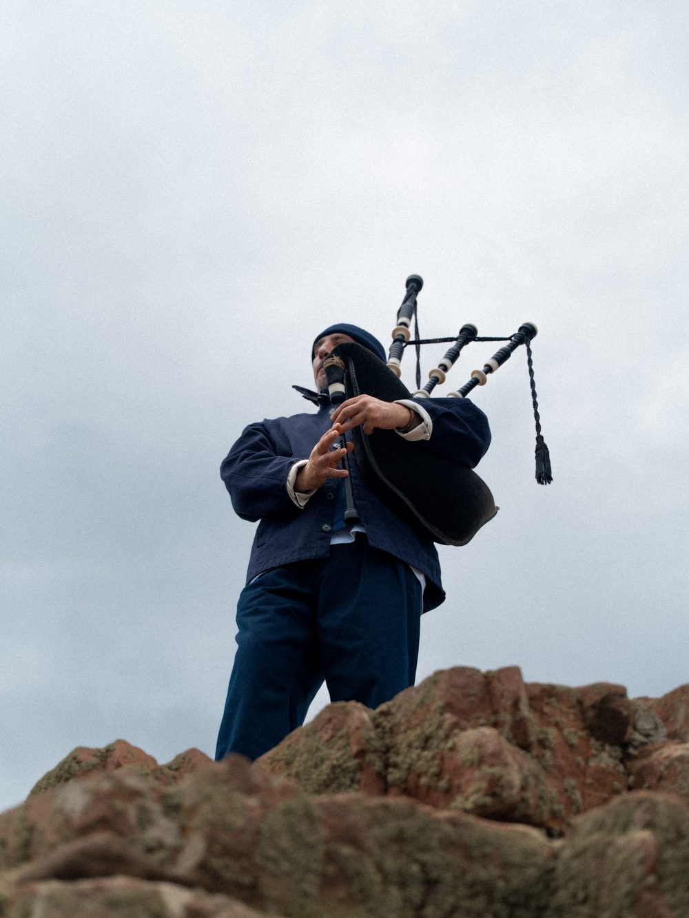 Le sonneur jouant au sommet des rochers, sa silhouette se détachant sur le ciel.