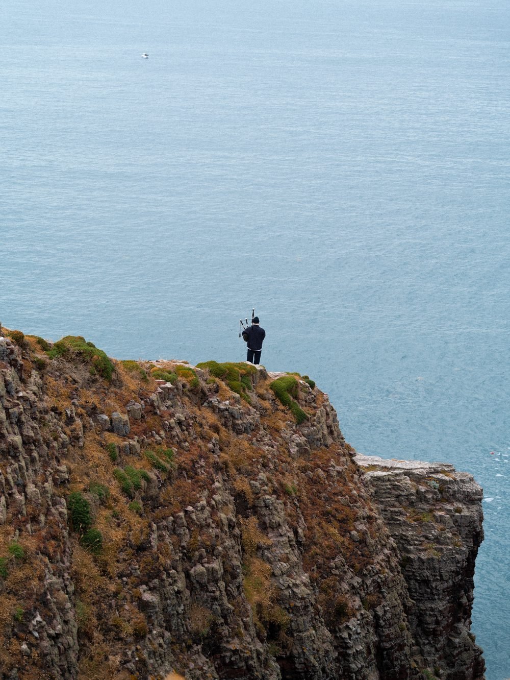Le sonneur minuscule au bord de la falaise, devant l'immensité de la mer.