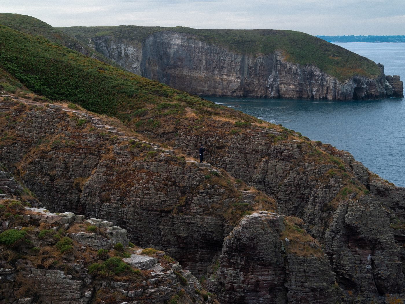 Vue large des falaises et de la mer, le sonneur minuscule sur le sentier.