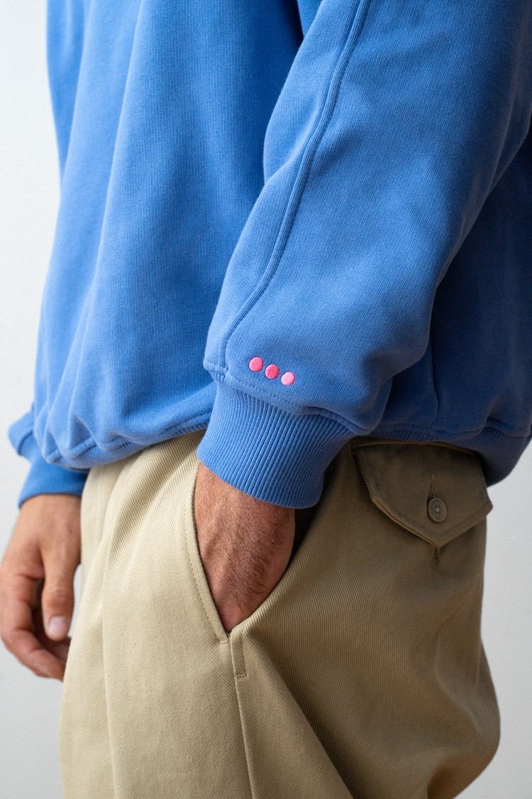 Détail de la manche du sweat bleu vif et de ses trois boutons rouges.