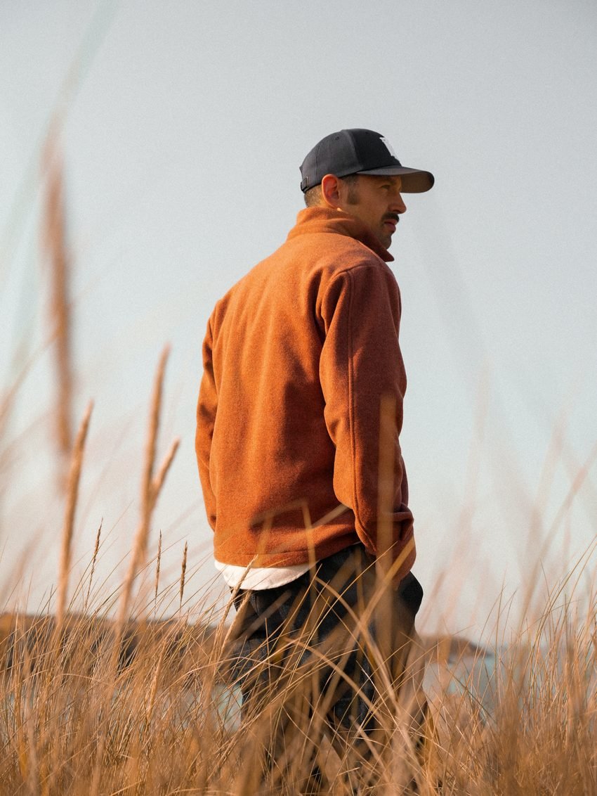 Homme de dos en polaire orange, au milieu des herbes hautes.