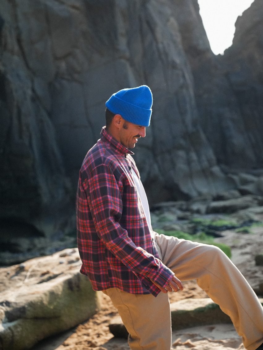 Homme en chemise à carreaux rouges et bonnet bleu, de profil dans les rochers.