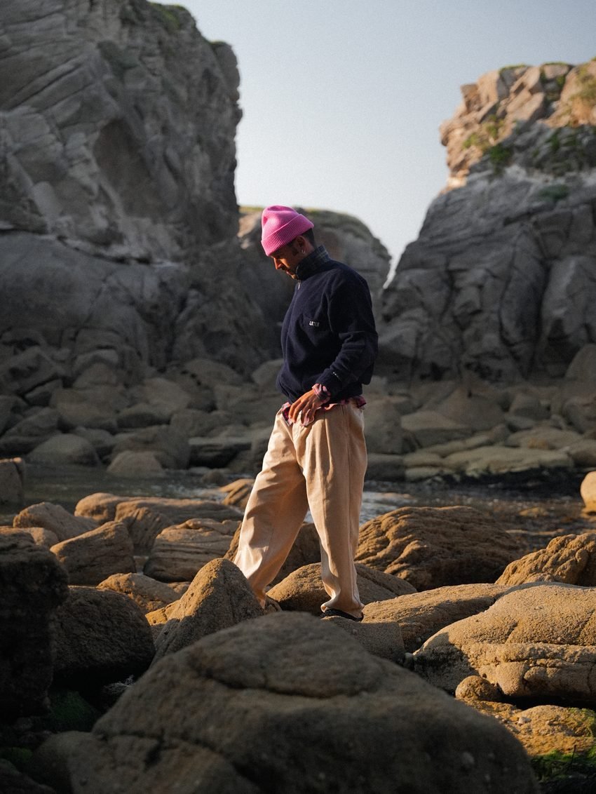 Homme en bonnet rose marchant sur les rochers au soleil couchant.