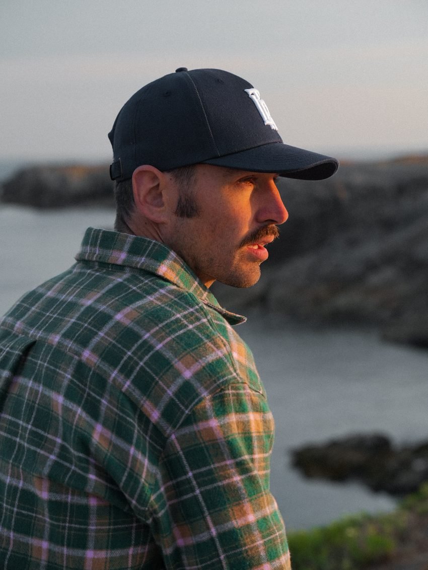 Portrait de profil, casquette noire et surchemise à carreaux verts.