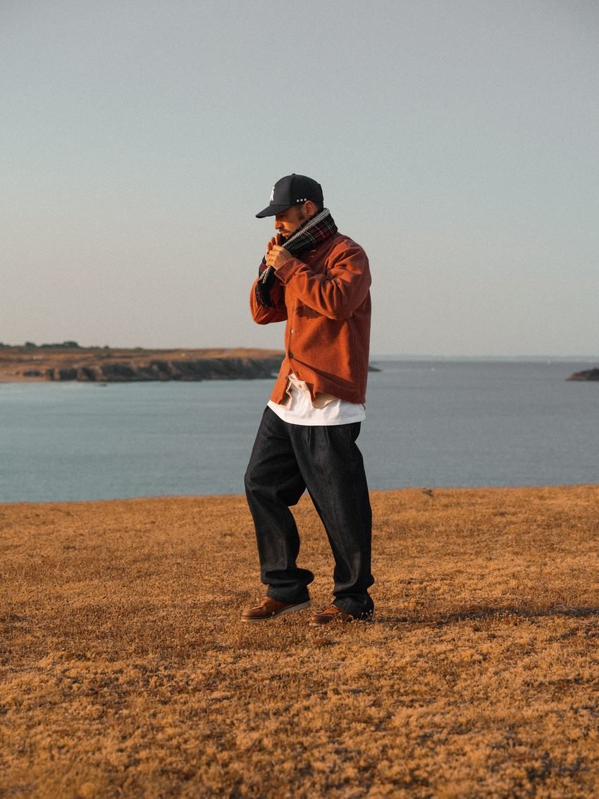 Homme en polaire orange et casquette, debout au milieu de la lande.