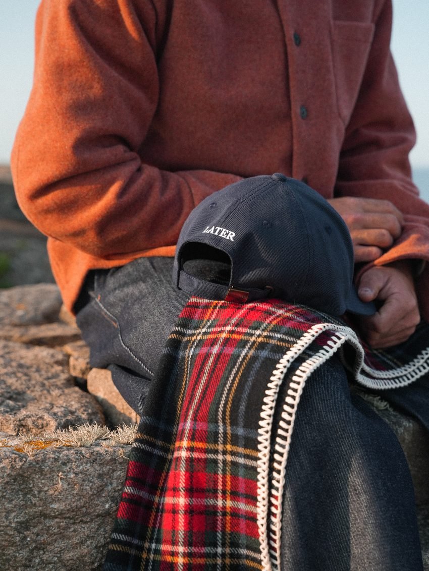 Détail : polaire orange, casquette et plaid à carreaux posé sur les genoux.