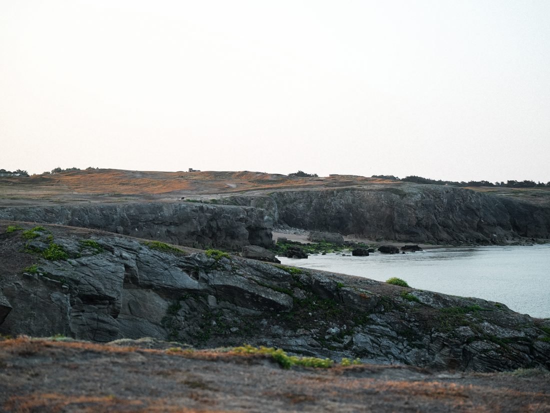 Vue large de la côte et d'une crique au soleil couchant.