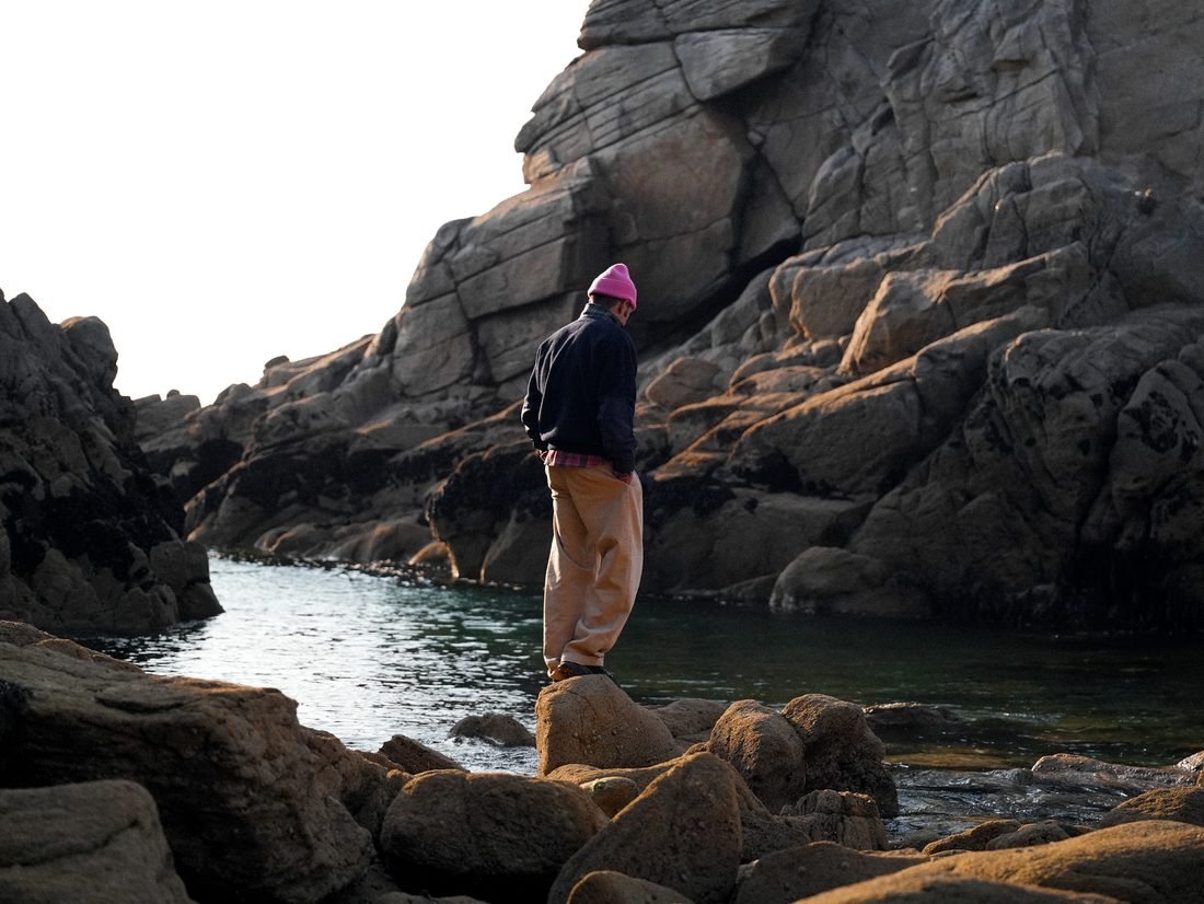 Homme debout sur un rocher au milieu des blocs de granit, bonnet rose.
