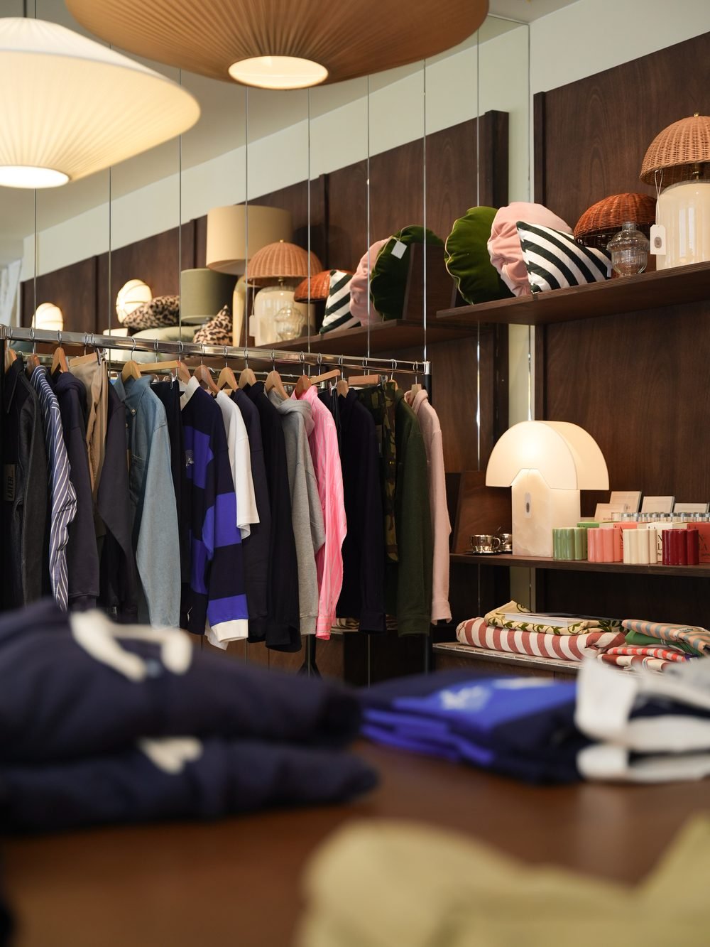 Intérieur de la boutique : portant de vêtements et étagères en bois garnies de lampes, pulls pliés au premier plan.