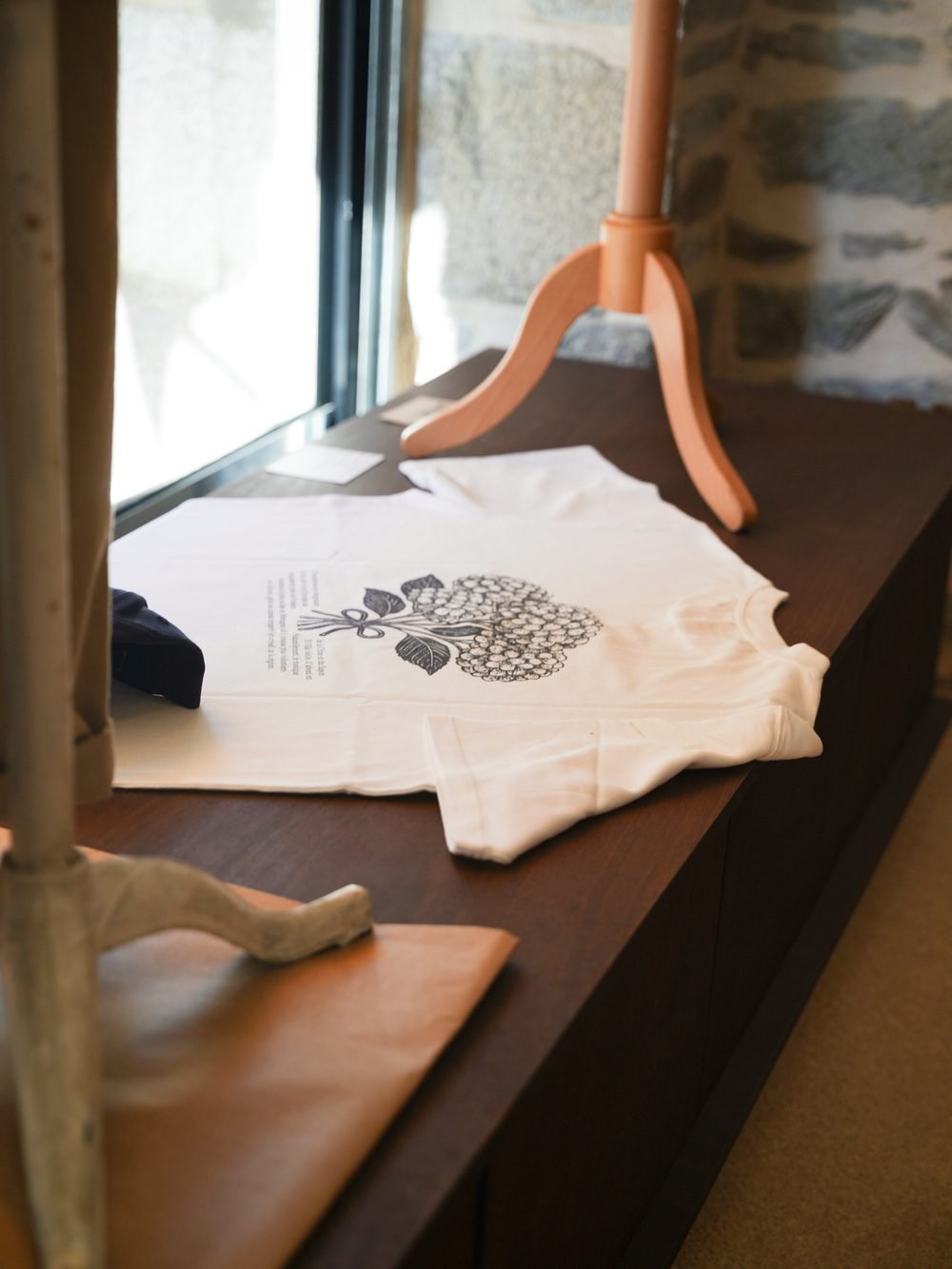 T-shirt écru à motif imprimé, posé sur une table en bois près de la vitrine.