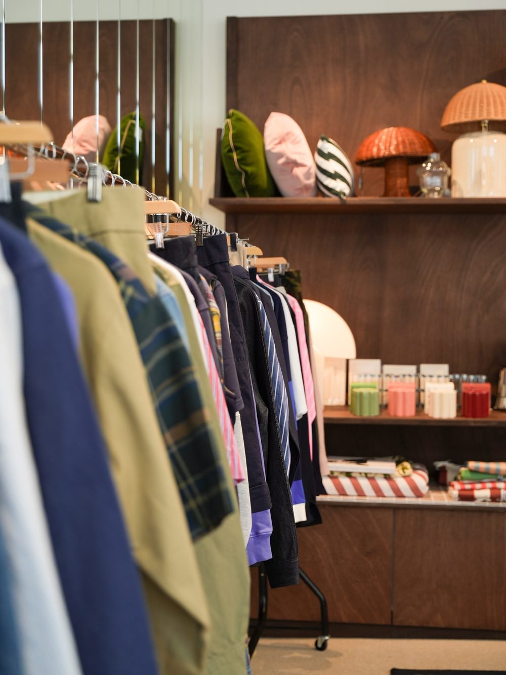 Portant de chemises et de vestes de la collection, devant les étagères en bois de la boutique.