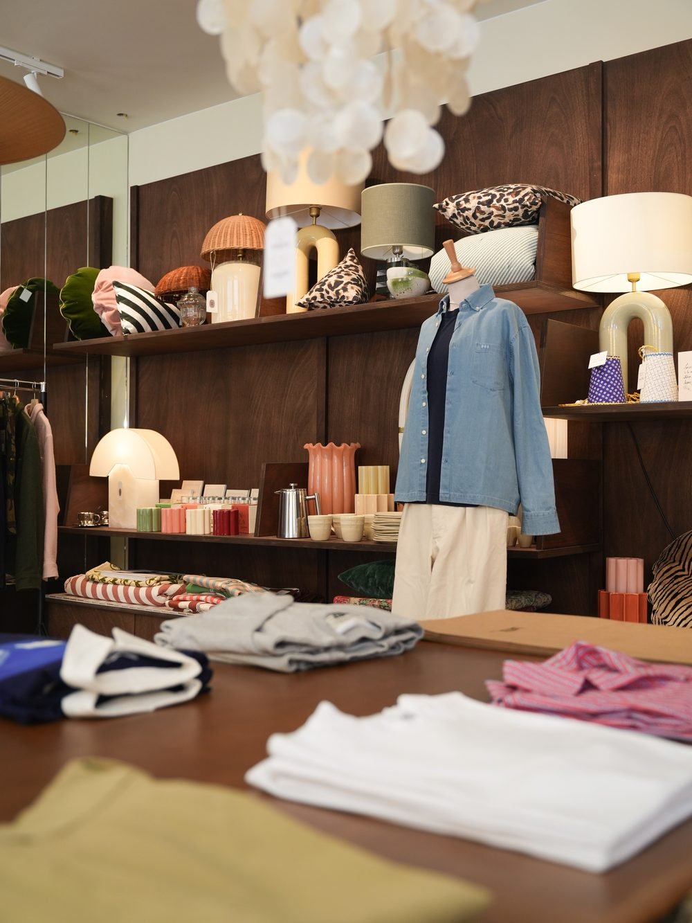 Mannequin en chemise en jean au fond de la boutique, table de vêtements pliés au premier plan.