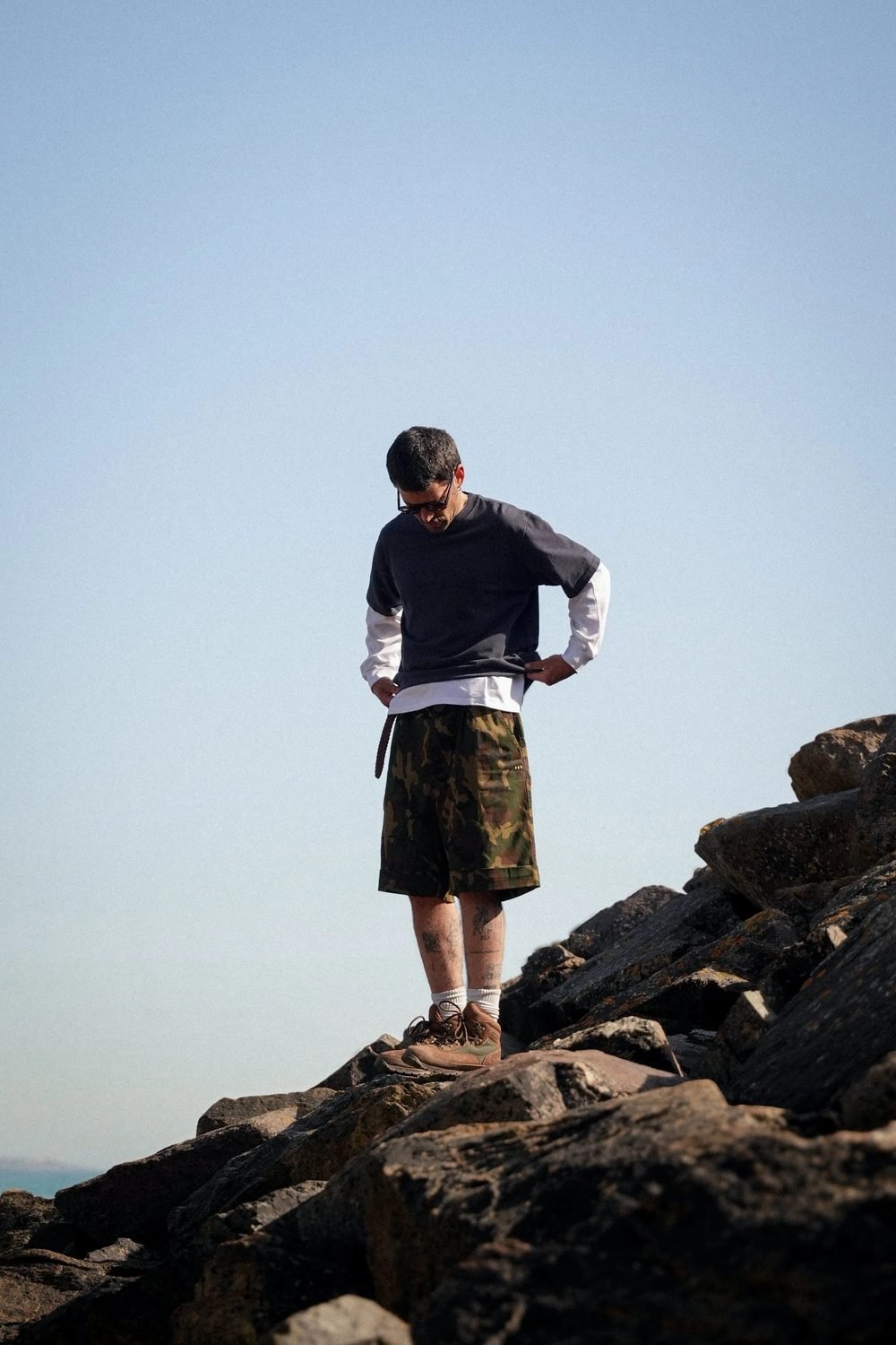 Homme debout sur les rochers en sweat bleu marine et short camouflage.