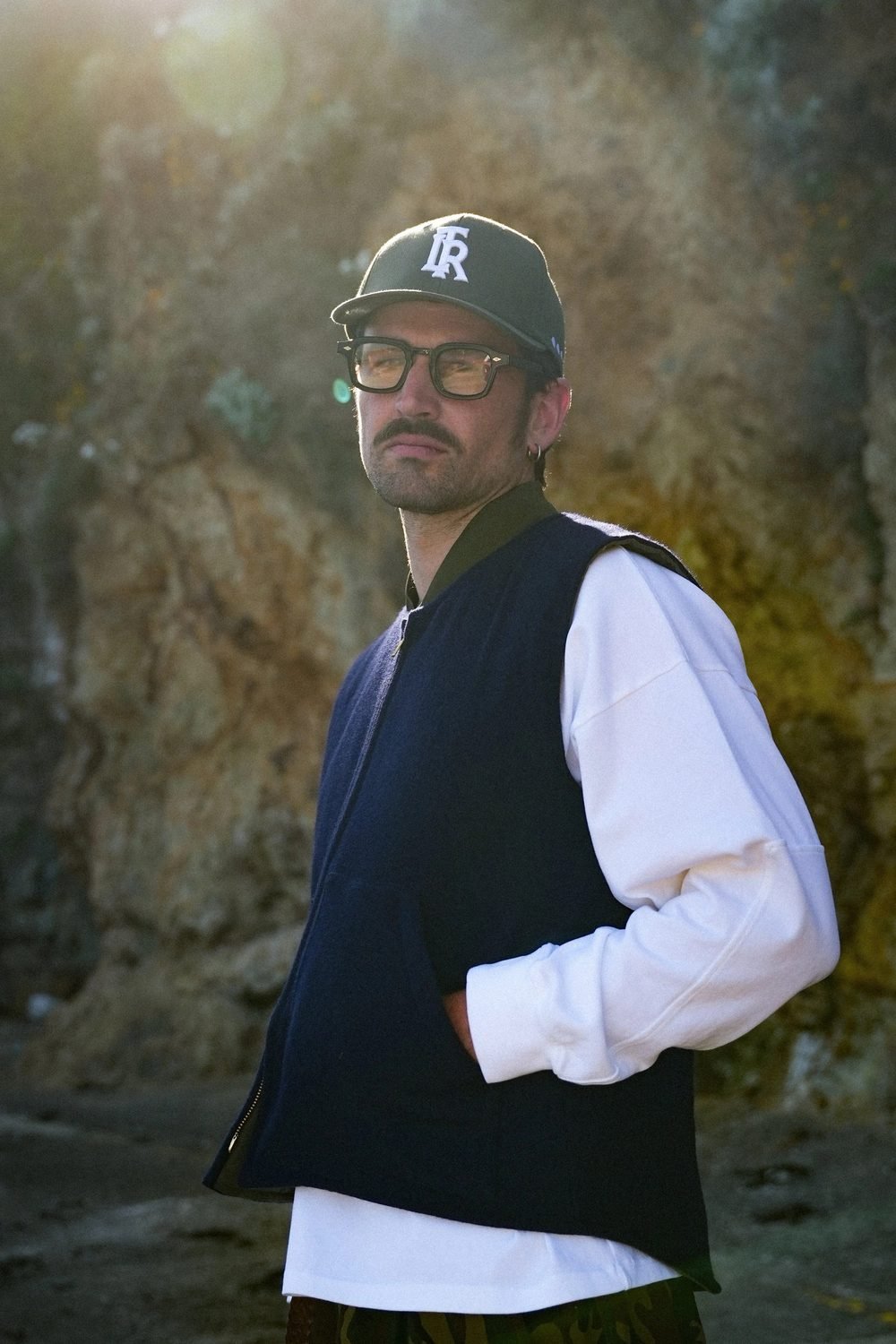 Portrait à contre-jour, casquette, gilet sans manches bleu marine sur chemise blanche.